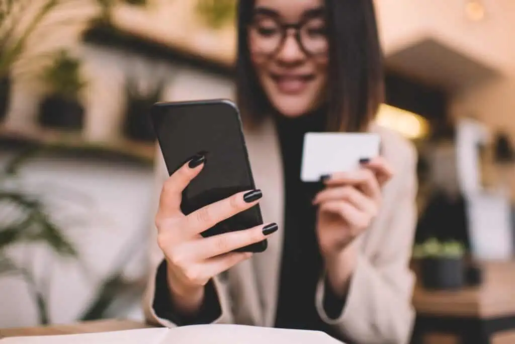 Girl with business card using smartphone in cafe